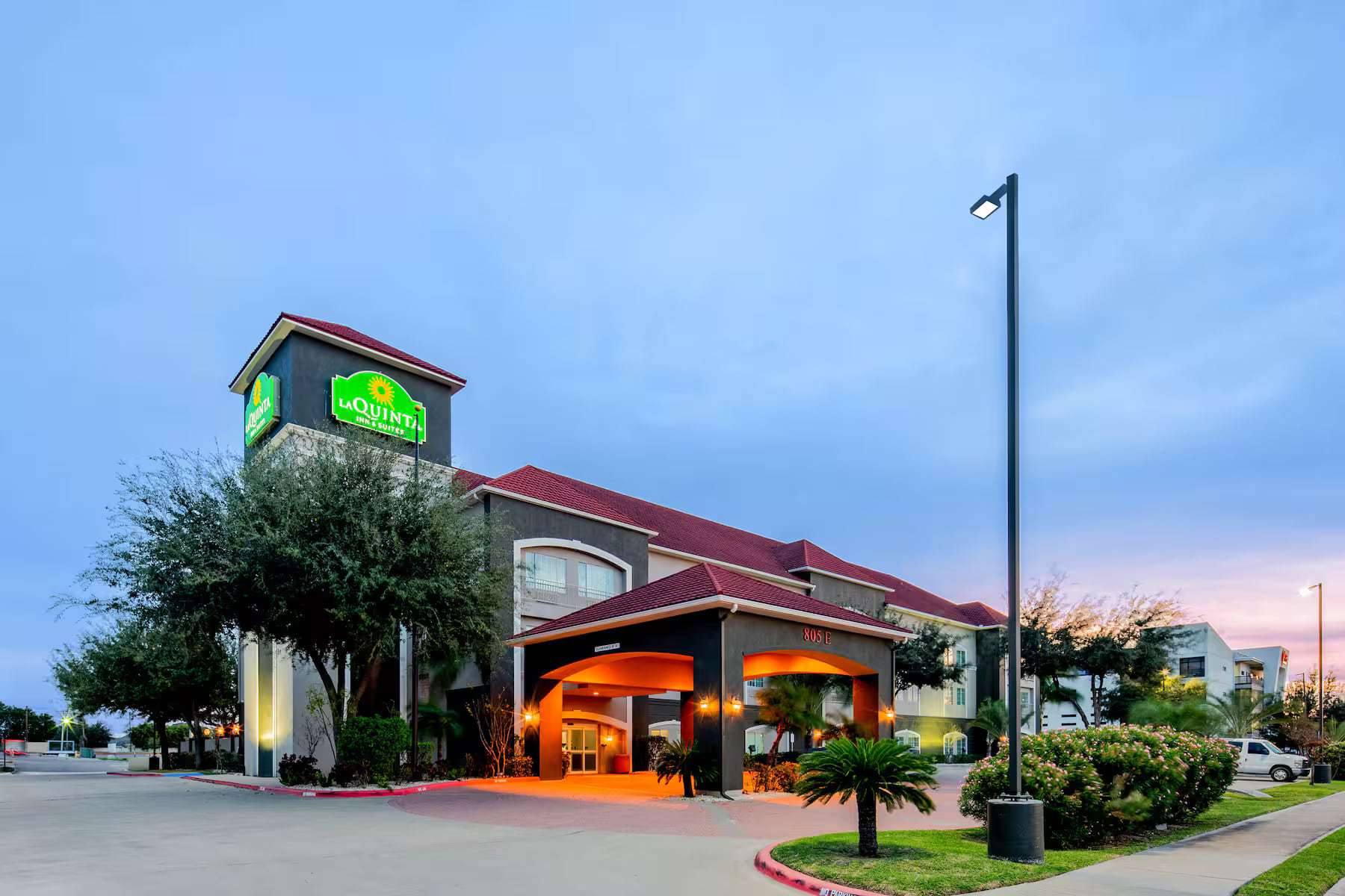 Hotel exterior at dusk with lit La Quinta sign and glowing porte-cochere entrance