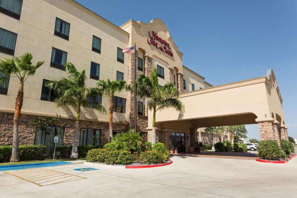 Hotel exterior by day with Hampton Inn & Suites sign, porte-cochère, palm trees and US flag