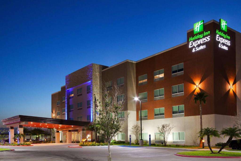 Holiday Inn Express & Suites Edinburg at dusk with lit sign, covered entrance and palm trees