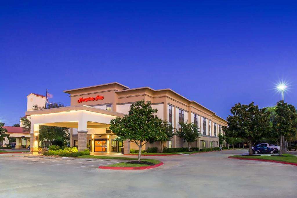 Three-story hotel exterior at dusk with lit Hampton Inn sign, porte-cochere and front parking lot