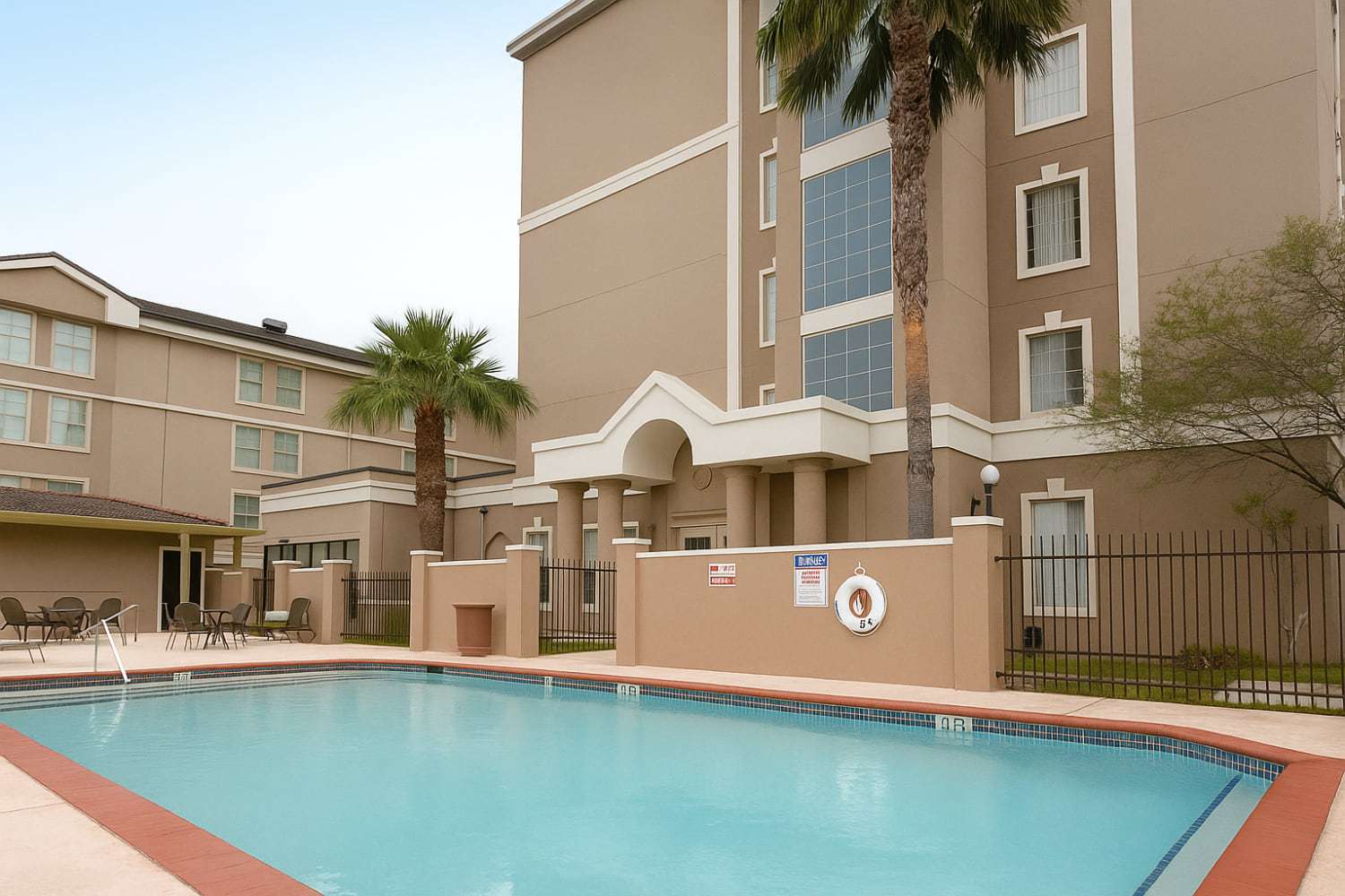 McAllen Plaza Hotel & Suites tower with an arched portico and palm trees rising behind the outdoor pool