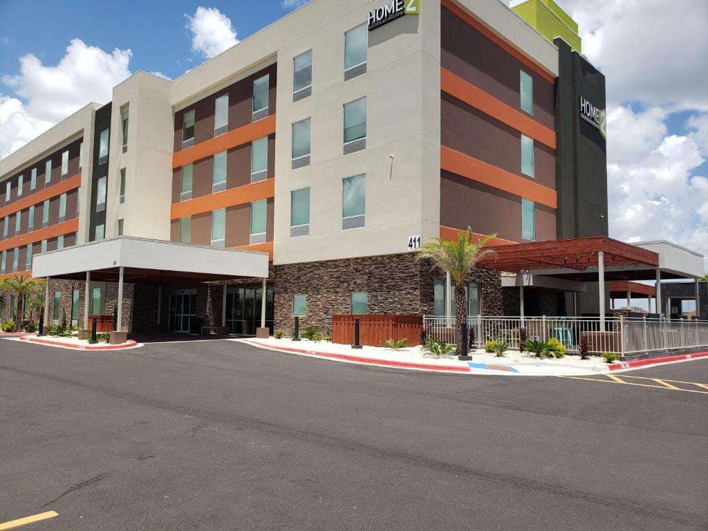 Home2 Suites Edinburg exterior with orange accents, stone base and covered entrance under blue sky