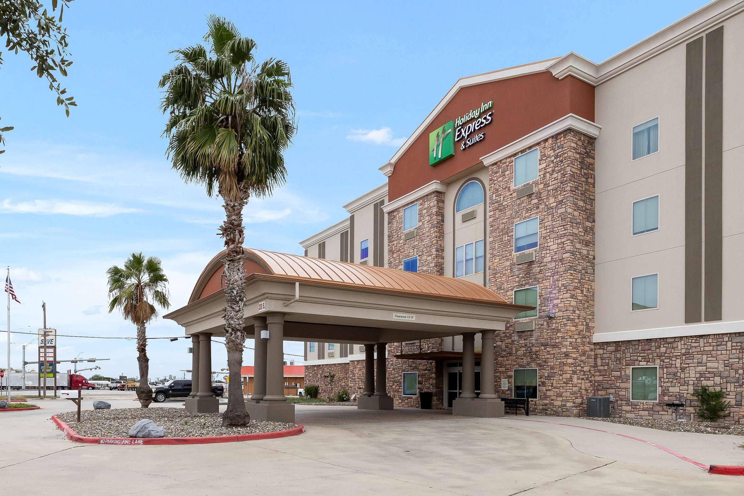 Hotel entrance with copper-roofed porte-cochere, tall palm trees and Holiday Inn Express & Suites sign