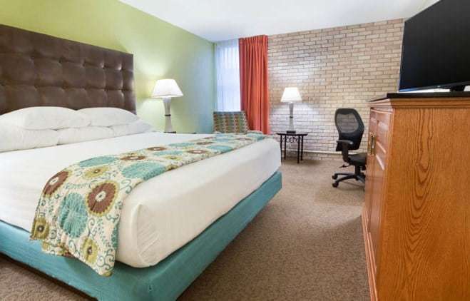 Traditional king room with tufted headboard, brick accent wall, work desk and dresser with flat-screen TV